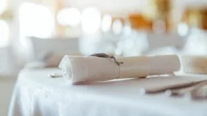 Photo d'ambiance restaurant : Table dressée avec serviettes en papier blanches pliées élégamment, couverts et verres, éclairage chaleureux